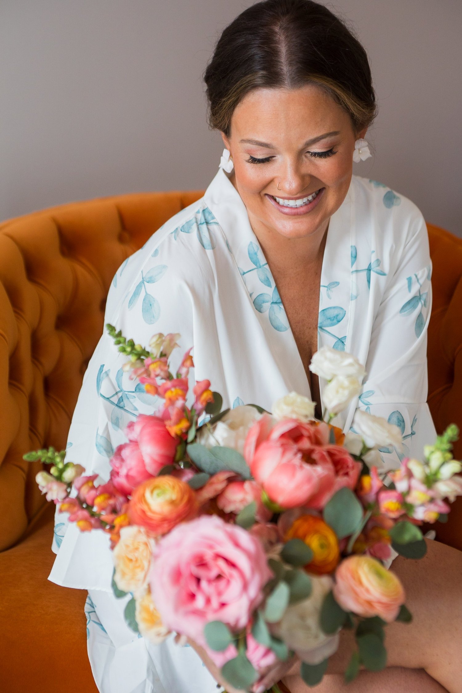 Bride in her robe holding a coral and blush bouquet